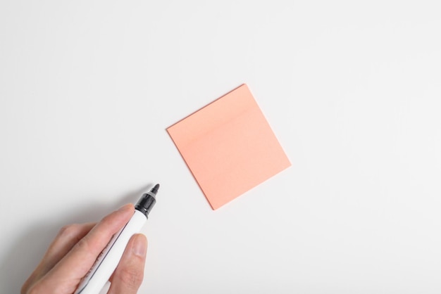 Closeup of a hand holding a marker and a selfadhesive blank sticker on a white background mockup