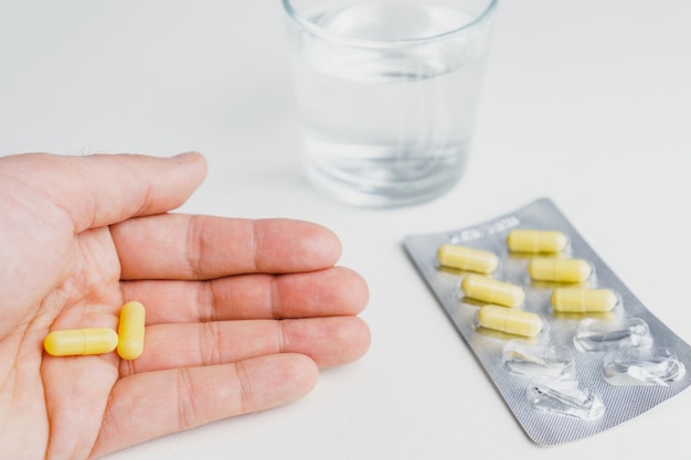 Closeup hand holding medicine capsule and glass of water at background Taking pill concept