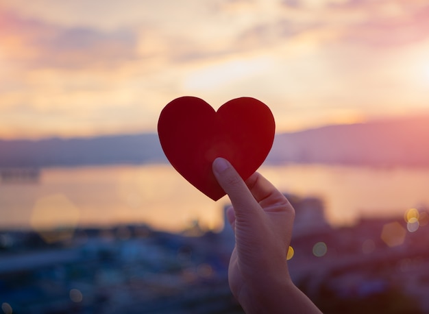 Foto mano del primo piano che tiene cuore rosso durante la priorità bassa di tramonto