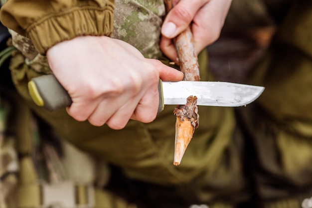 Мужчина-охотник крупным планом с ножом перерезал деревянную палку для костра в лесу xA