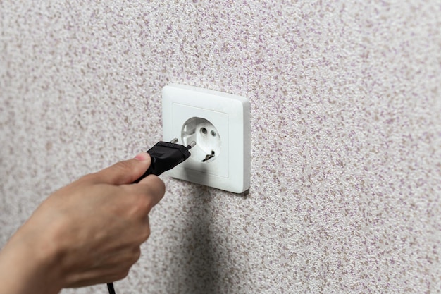 Closeup of a hand inserting a black plug into a white socket