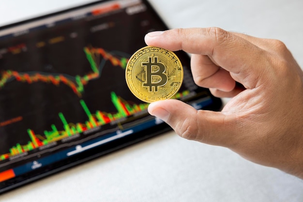 Closeup hand of man holding crypto coin on chart in tablet background Blockchain technology finance future Male hold bitcoin concept about business finance trade economy banking investment