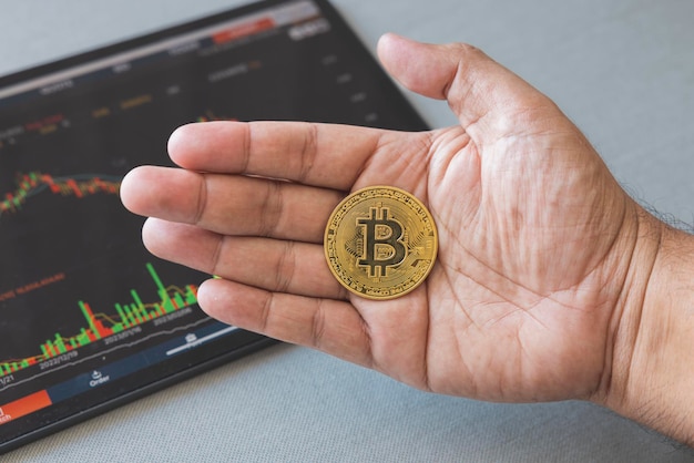 Closeup hand of man holding crypto coin on chart in tablet background Blockchain technology finance future Male hold bitcoin concept about business finance trade economy banking investment