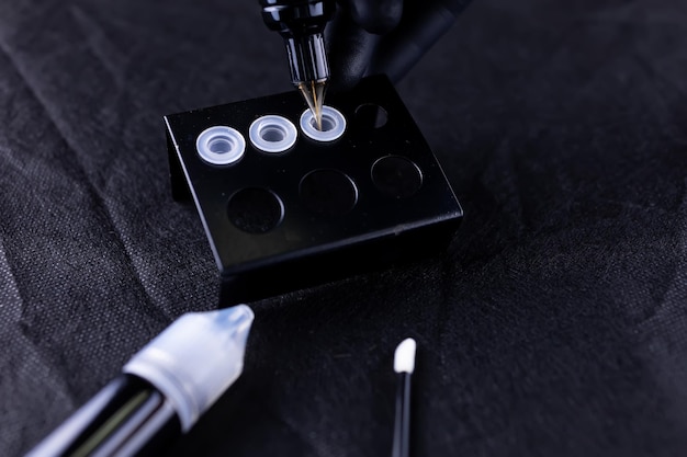 Closeup of the hand of the permanent makeup artist of the eyebrows which is gaining pigment in the cartridge of the tattoo machine