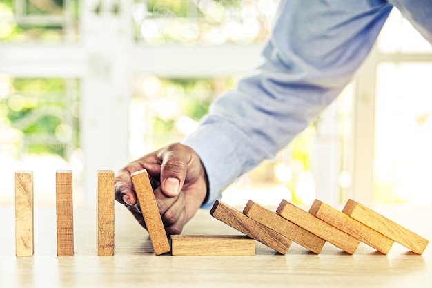 La mano del primo piano impedisce al blocco di legno di non cadere concetti di domino di gestione del rischio finanziario e pianificazione strategica e piano di sfida aziendale