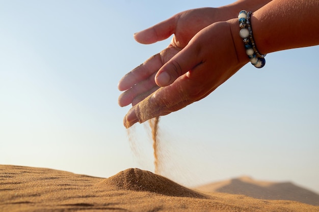 Closeup hand releasing dropping sand Sand flowing through the hands against golden desert Summer holiday vacation