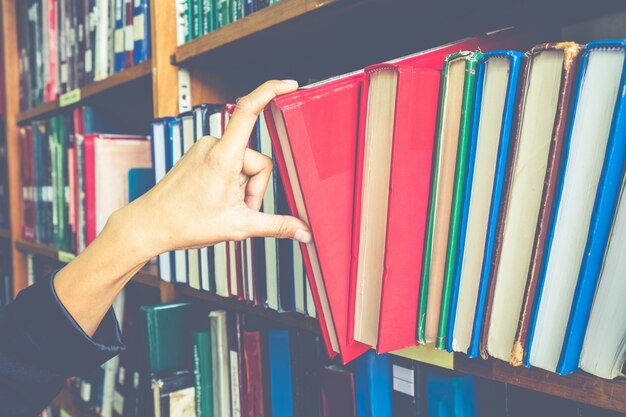 Photo closeup hand selecting book from a bookshelf