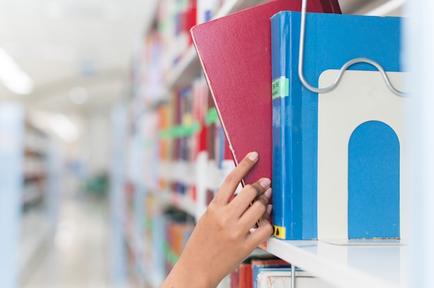 Mano del primo piano che seleziona libro da uno scaffale per libri