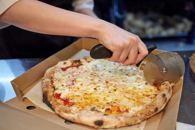 Closeup hand van chef-kok bakker in witte uniform snijden pizza in de keuken.