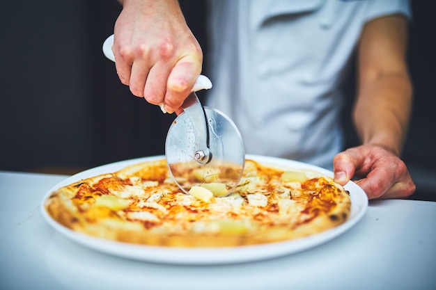 Closeup hand van chef-kok bakker in witte uniform snijden pizza in de keuken.