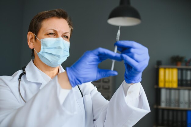 Closeup hand van vrouwelijke arts of wetenschapper in doktersuniform met gezichtsmasker beschermend in laboratorium met medicijn vloeibare vaccins flacon fles coronavirus of COVID19 concept