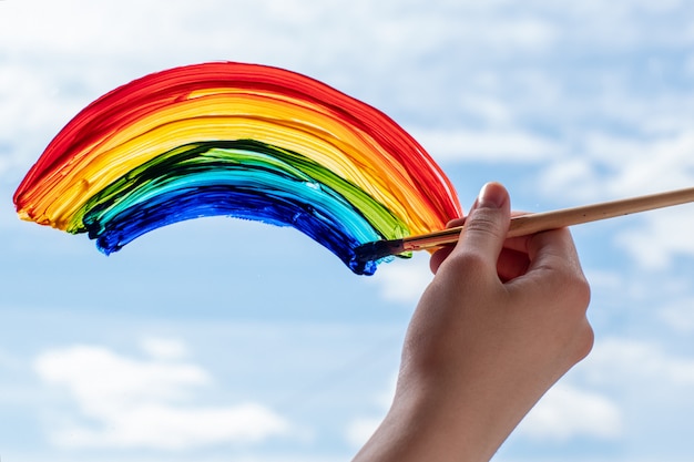 Foto primo piano di una mano con un pennello dipinge un arcobaleno