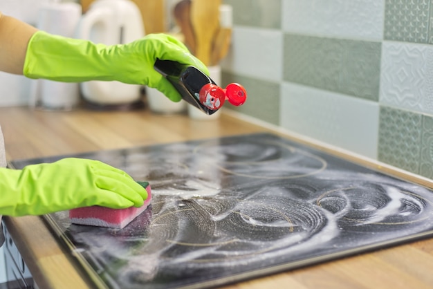 Closeup of hand woman cleaning modern cooking glass ceramic electric surface with sponge and detergent