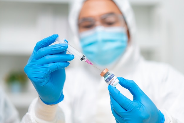 Primo piano della mano della donna medico dpi suite uniforme che indossa la maschera protettiva in laboratorio tenere medicina vaccino liquido