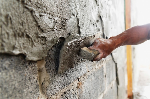 Крупным планом рука работника штукатурки цемента на стене на строительной площадке