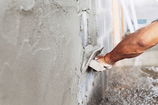 Крупным планом рука работника штукатурки цемента на стене на строительной площадке