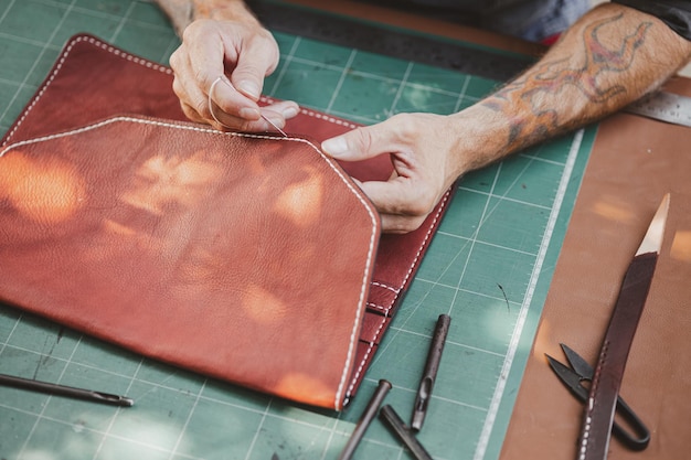 Closeup hand working process leather handcraft in the leather workshop Man holding crafting tool and working He is sewing hammer to make a walet Tanner in old tannery