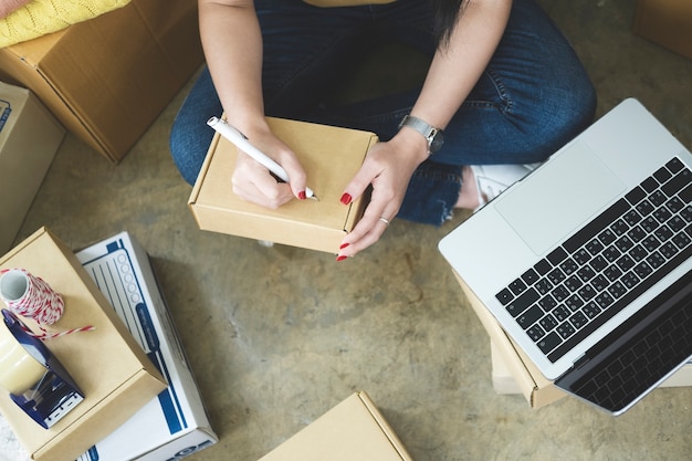 Closeup hand of young woman writing address on parcel box  for delivery order to customer, shipping and logistic, merchant online and seller, business owner or SME, online shopping.