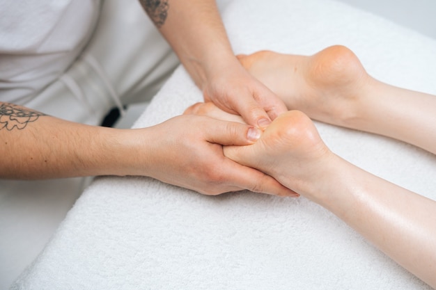 Closeup handen van mannelijke masseur die voeten masseert aan jonge vrouw liggend op massagetafel in spa salon