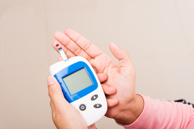 Closeup handen vrouw glucose test niveau controleren met bloed op vinger door glucometer thuis