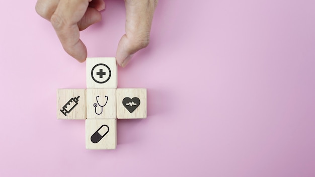 Photo closeup hands arranging wood cube with medical symbol on pastel pink background