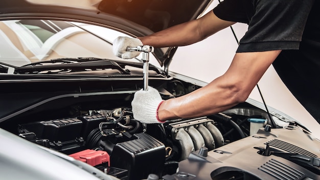 自動車整備士のクローズアップの手は、自動車のガレージで車のエンジンを修理するためにレンチを使用しています
