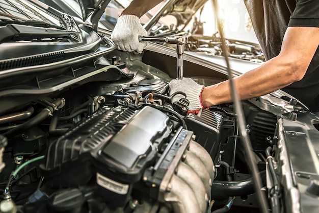 Mani del primo piano del meccanico automatico che utilizzano la chiave per la manutenzione del motore dell'auto