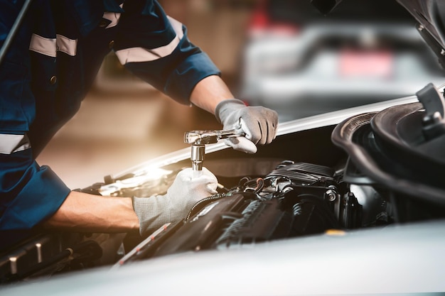 Primo piano le mani del meccanico che utilizza la chiave per la manutenzione del motore dell'auto