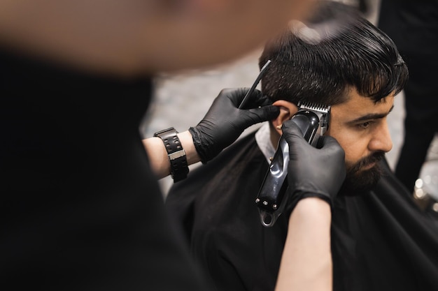 Primo piano delle mani di un barbiere che taglia i capelli sulla testa di un uomo con un clipper