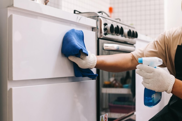 Closeup of hands cleaning kitchen cabinets with detergent spray bottle and cloth