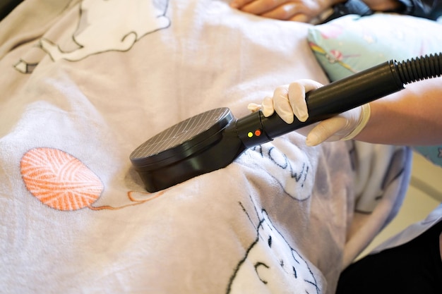 Closeup hands of doctor using electrical muscle stimulation at elderly patient's legs in blankets