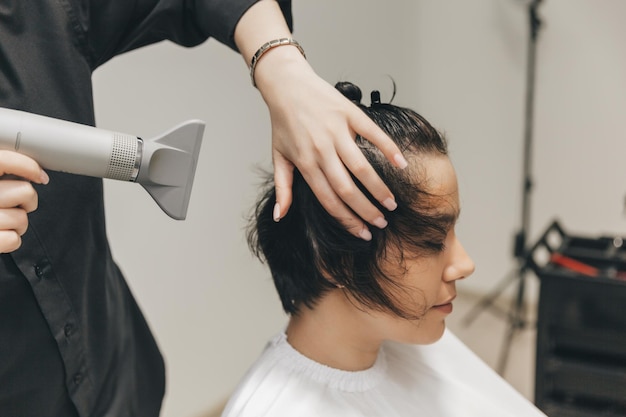 Closeup of the hands of a hairdresser drying women's hair with a hairdryer short haircut and styling