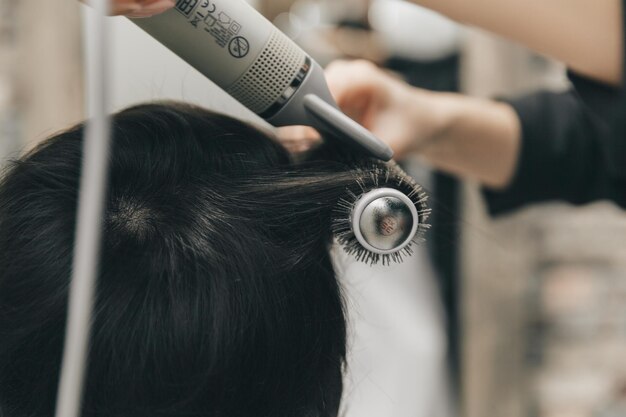 ヘアドライヤーの短いヘアカットとスタイリングで女性の髪を乾燥させる美容師の手の接写