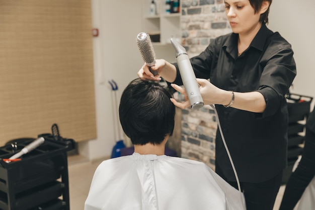 Closeup of the hands of a hairdresser drying women's hair with a hairdryer short haircut and styling