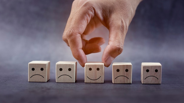 Mani del primo piano che tengono l'icona della faccina sorridente sul concetto di leadership di valutazione del servizio di cubo di legno