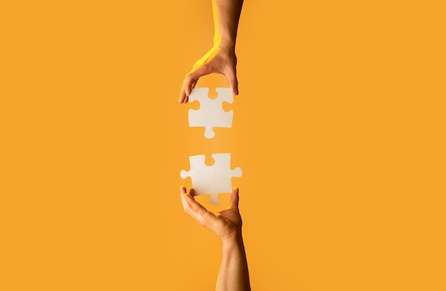 Photo closeup hands of man connecting jigsaw puzzle two hands trying to connect couple puzzle with yellow background hand connecting jigsaw puzzle man hands connecting couple puzzle piece