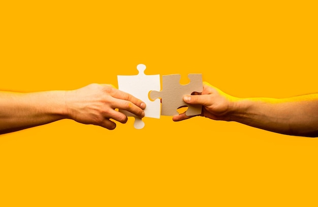 Closeup hands of man connecting jigsaw puzzle Two hands trying to connect couple puzzle with yellow background Hand connecting jigsaw puzzle Man hands connecting couple puzzle piece