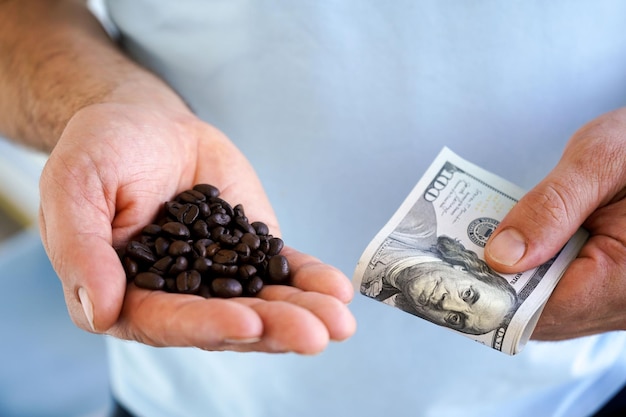 コーヒー豆と 100 ドル札を彼の手で保持している男の手のクローズ アップ食品価格の上昇の概念、世界的な経済危機