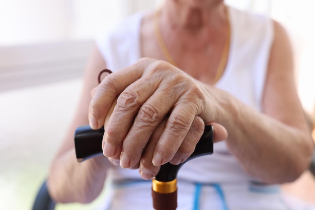 Closeup of hands of old woman holding walking cane senior female using supporting stick old age