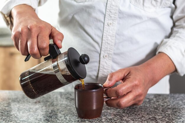 Closeup of hands pouring a cup of coffee brewed in a French press