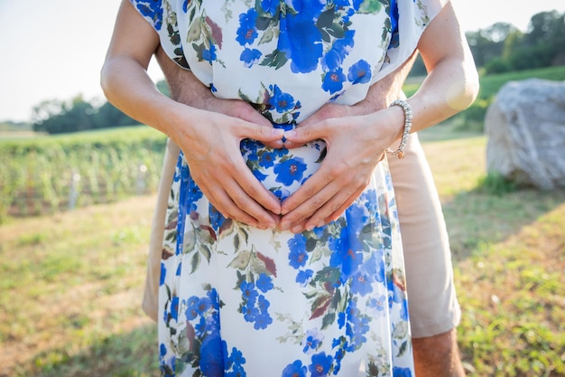 妊娠中の将来の母親の手のクローズ アップと彼女のパートナーは、妊娠と妊娠中のカップルのハート シンボルの概念を作る