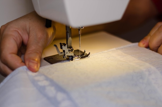ミシンで白い布を縫う裁縫師の手のクローズアップ
