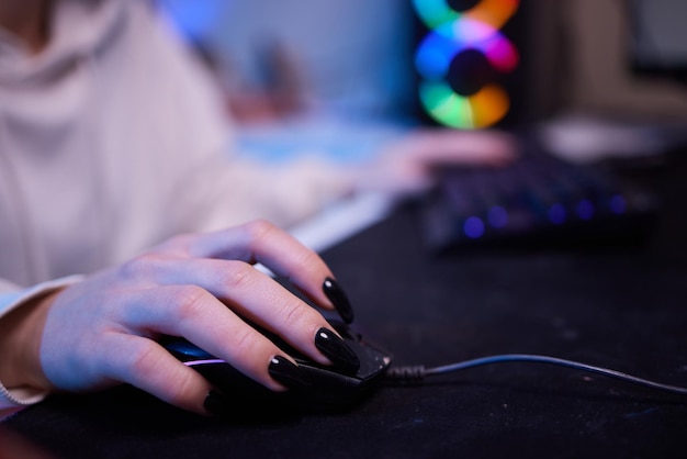 Руки крупным планом сняты азиатской девушкой-геймером, использующей клавиатуру и контроллер мыши, играющими в видеоигры с компьютером с неоновым светом на столе дома.