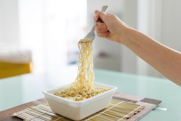 Photo a closeup of hands showing the consumption of junk food showing instant noodles with a fork in the foreground