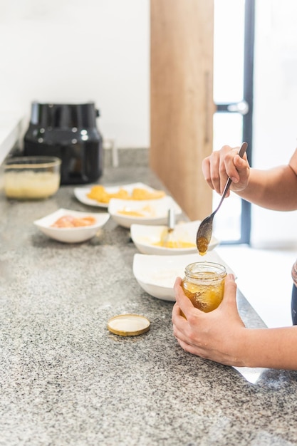 Closeup of hands taking honey from a container next to other ingredients on the kitchen counter