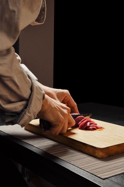 Photo closeup of hands of unrecognizable woman slicing raw beef meat on thin slices