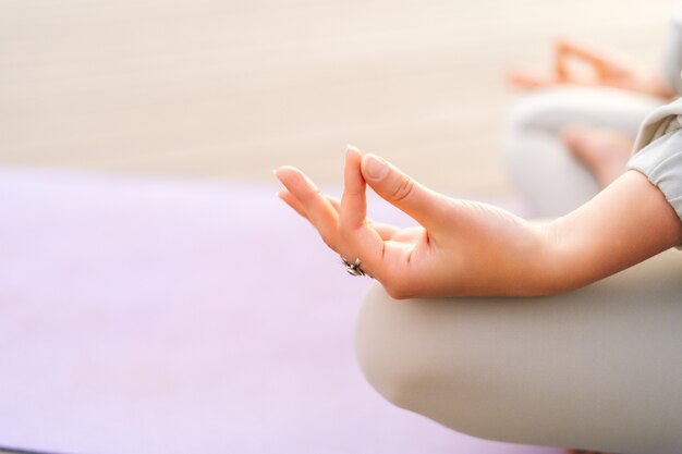 Closeup hands of unrecognizable young woman meditating on yoga mat in lotus position holding hand on