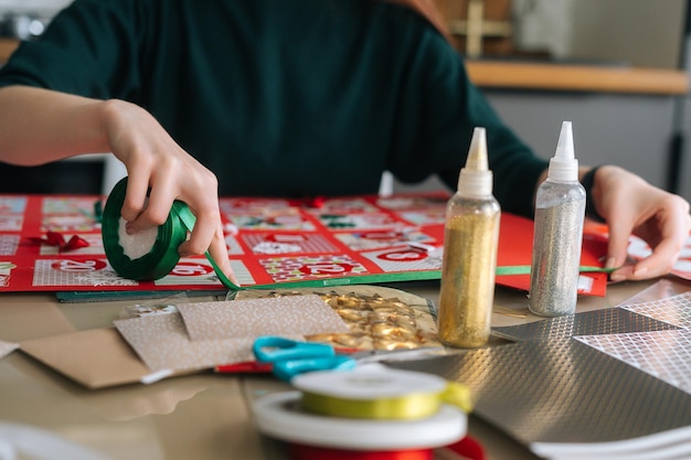 Closeup hands of unrecognizable young woman using holiday ribbon to frame board with advent calendar envelopes at home