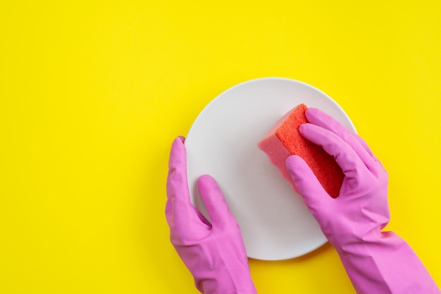 Closeup hands wearing in latex gloves holding a kitchen sponge and plate.