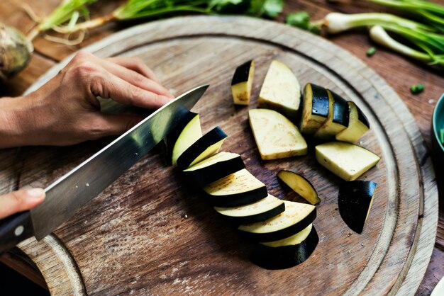 Closeup of hands with knife cutting fresh organic eggplant